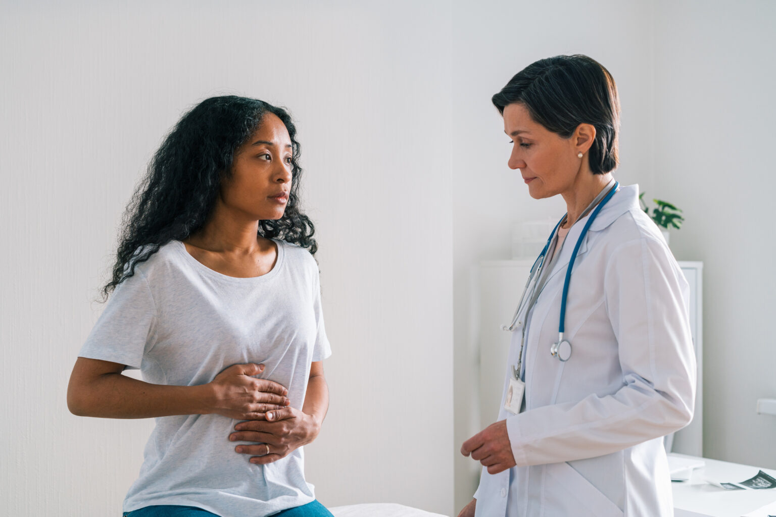 African-american female patient touching belly and telling a mature worried doctor about stomachache at hospital appointment. Healthcare specialist showing concern about symptoms